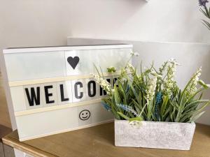 ein Willkommensschild auf einem Tisch mit Blumen in der Unterkunft Twin Pines in Kenley