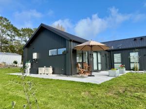 a black house with an umbrella and a bench at The Mann Homestay, Premium King Room with Private Ensuite, Near Waihi & Coromandel in Waihi