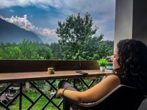 a woman sitting at a table looking out a window at La Hostelgia in Manāli