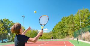 a young boy holding a tennis racket on a tennis court at Domaine Le Petit Lac in Moustiers-Sainte-Marie
