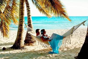 two people sitting in a hammock on the beach at CARIBBEAN DREAM OCEAN view VILLAS & Apartments with POOL PLAYA Los Corales in Punta Cana