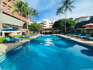 a large swimming pool with blue chairs and palm trees at Nautical Inn in Pattaya