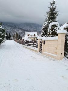 a snow covered street with a house and a fence at Cabana Antonio&Thea in Poiana Ţapului