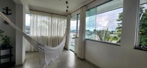 a swinging hammock in a room with a large window at Cobertura Duplex, PiSCiNA, Churrasqueira e Alegria in Guaratuba