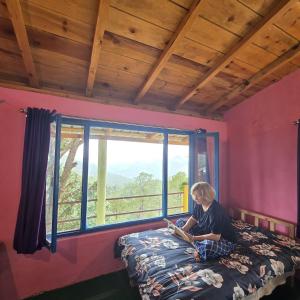 a man sitting on a bed in a room with a window at The Himalayan Heaven Homestay, Binsar in Binsar