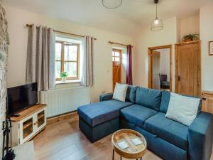 a living room with a blue couch and a tv at Thornycroft Cottage in Llanvair Discoed