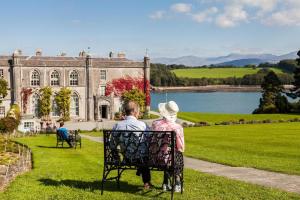a man and woman sitting on a bench in front of a castle at Tyddyn-Hendre in Llanfairpwllgwyngyll
