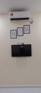 a flat screen tv on a white wall with pictures at Roomstay Cheq Ayoh Pantai Penarik Setiu in Kampong Ru Sepuloh
