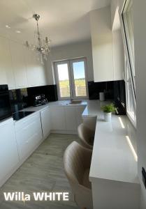 a white kitchen with white cabinets and a chandelier at Dom Michałki Luksusowa willa z ogrodem in Michalki