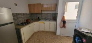 a kitchen with white cabinets and a refrigerator and a window at Maison piscine privée in Bū Shammah