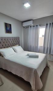a bedroom with a large bed with white sheets and a window at Acomodação Quartzo Rosa - Apartamento Completo in Palhoça