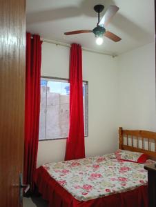 1 dormitorio con 1 cama con cortinas rojas y ventana en Casa da Nataliana, en Cabo Frío