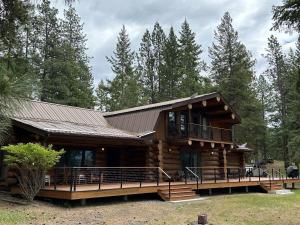 a log cabin with a deck in the woods at Living Well Lodge with Panoramic Views in Moyie Springs