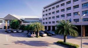 a parking lot in front of a building with palm trees at Western Grand Hotel Ratchaburi in Ratchaburi