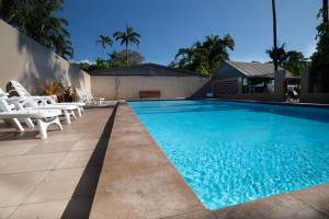 una piscina con sillas blancas y una casa en Tropical Hibiscus Caravan Park, en Mission Beach