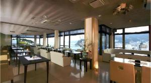 a restaurant with tables and chairs and large windows at Tsukino Sumika Atami Juraku Hotel in Atami