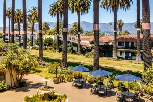 un complejo con palmeras, mesas y sombrillas en Hotel Milo Santa Barbara en Santa Bárbara