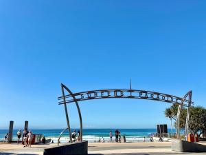 Un arco de metal en la playa con gente caminando por la playa. en 1BR Apartment Heated pool, en Gold Coast