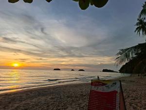 a sunset on a beach with a sign in the sand at Crazy Bananas in Trat +11 photos