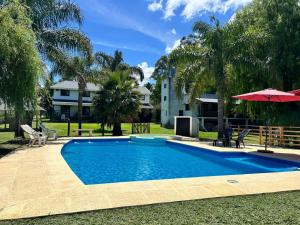 a swimming pool with an umbrella and chairs and a house at Cabañas del Paraiso in Colón