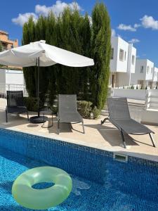 a swimming pool with chairs and an umbrella and a greenogieogieogieogieogie at Villa 2 Golden View in Peyia