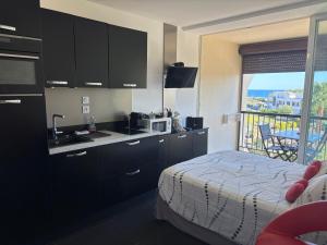 a kitchen with black cabinets and a bed and a balcony at BAGATELLE NATURISTE HELIOPOLIS clim ascenseur vue mer parking privé in Cap d'Agde