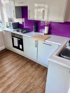 a kitchen with white cabinets and purple walls at Denzels Den Apartment 2 in Llandudno Junction