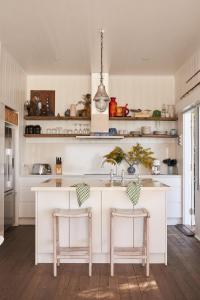 a kitchen with white cabinets and a island with two stools at Bay Properties The Beach House in Yamba
