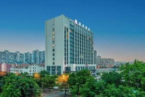 a tall white building with trees in front of a city at Echarm Hotel Liuzhou Liunan Wanda Plaza in Liuzhou