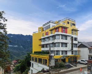 a tall yellow and white building with mountains in the background at Lestar Hotel Sapa in Sa Pa
