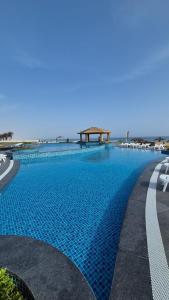 a large blue swimming pool with chairs and the ocean at Arabian Sea Resort Salalah in Mirbāţ