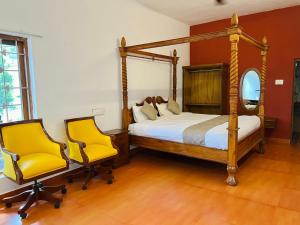 a bedroom with a four poster bed and two yellow chairs at Queen's Heritage in Yercaud +9 photos