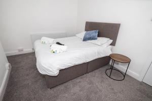 ein Bett mit weißer Bettwäsche und Kissen sowie einem Hocker in der Unterkunft Spacious 3BR Swansea House near City Centre in Swansea