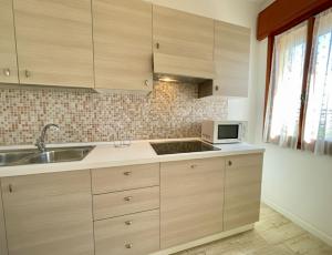 a kitchen with wooden cabinets and a sink and a microwave at Spacious apartment near the beach in Porto Santa Margherita di Caorle