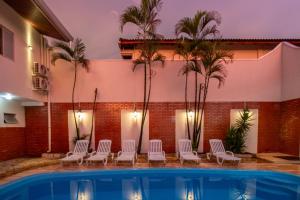 une piscine avec des chaises blanches et des palmiers dans l'établissement Nana Suites, à Foz do Iguaçu