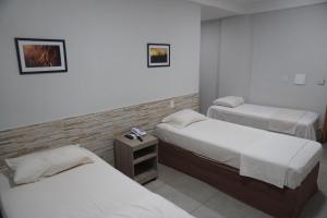 a hotel room with two beds and a night stand at Hotel Portal dos Cerrados in Uruçuí