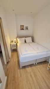 a white bed in a room with a wooden floor at Deichliebe 3 - gemütlich, zentral und modern- Inklusive privater Stellplatz im Parkhaus 2min zu Fuß entfernt in Bremerhaven