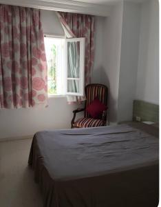 Un dormitorio con una cama y una silla y una ventana. en Aux jardins de Hammamet, en Hammamet