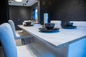 ein Tisch mit weißen Stühlen und schwarzen Tassen darauf in der Unterkunft Villa Emma - Modern Bungalow with EV Point, Free Parking & Workspace in Northampton