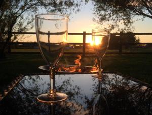 two wine glasses sitting on a table with the sunset in the background at Oxford Riverside Glamping in Oxford