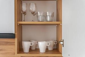 un estante con copas de vino y tazas. en Apartament Odrzańskie Tarasy, Klimatyzacja, PW INVEST HOME, en Krapkowice