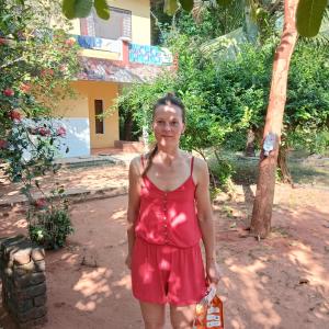 Una donna con un vestito rosso in piedi davanti a una casa di Tranquality ad Auroville