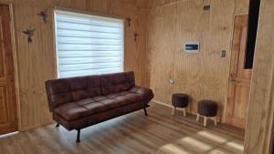ein braunes Ledersofa in einem Zimmer mit Fenster in der Unterkunft Cabaña Vista DIvisadero in Coihaique