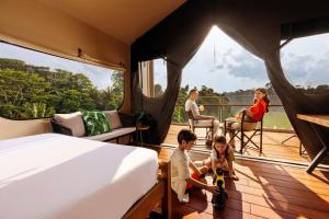 a family in a room with a bed and a balcony at Colugo Camp, Mandai Wildlife East in Singapore
