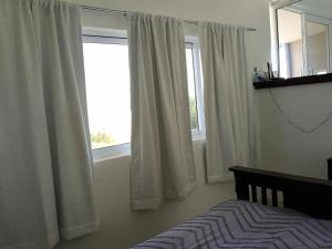 a bedroom with white curtains and a bed and a window at Desert Blue in Ensenada