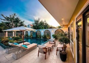 a house with a swimming pool with chairs and an umbrella at Hometown Signature Retreat Villa Hoi An in An Bang