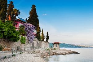 a house with purple flowers on a stone wall next to the water at Apartments Camellia & Magnolia in Volosko