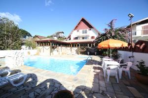 a house with a swimming pool with chairs and an umbrella at Hotel JB in Campos do Jordão