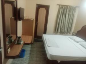 Un dormitorio con una cama blanca y un espejo. en Hotel Valluvar, en Karūr