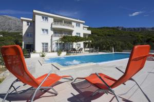 two chairs and a swimming pool in front of a building at Apartmani Villa Athina in Tučepi